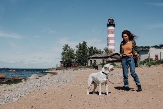 海滩上，一位带着拉布拉多猎犬的女人站在条纹灯塔旁