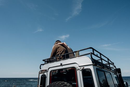 Free A couple enjoying a romantic moment on top of a rugged SUV by the sea under a clear blue sky. Stock Photo