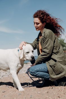 阳光明媚的海滩上，一名女子正抚摸着一只拉布拉多猎犬