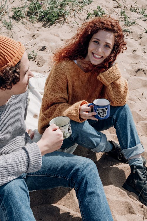 Man and Woman Holding Mugs While Sitting on Sand