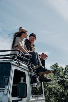 A couple sitting on the roof of an SUV, embracing adventure and nature.