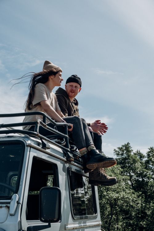 Free A couple sitting on the roof of an SUV, embracing adventure and nature. Stock Photo