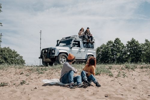 Free Group of friends enjoying leisure time outdoors with SUV on sandy terrain. Stock Photo
