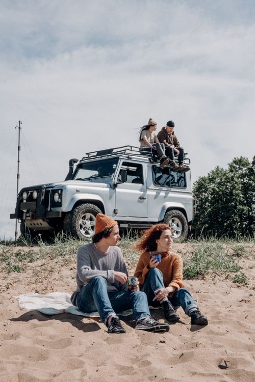 Free Young friends enjoying a sunny day by the beach with an SUV in the background. Stock Photo