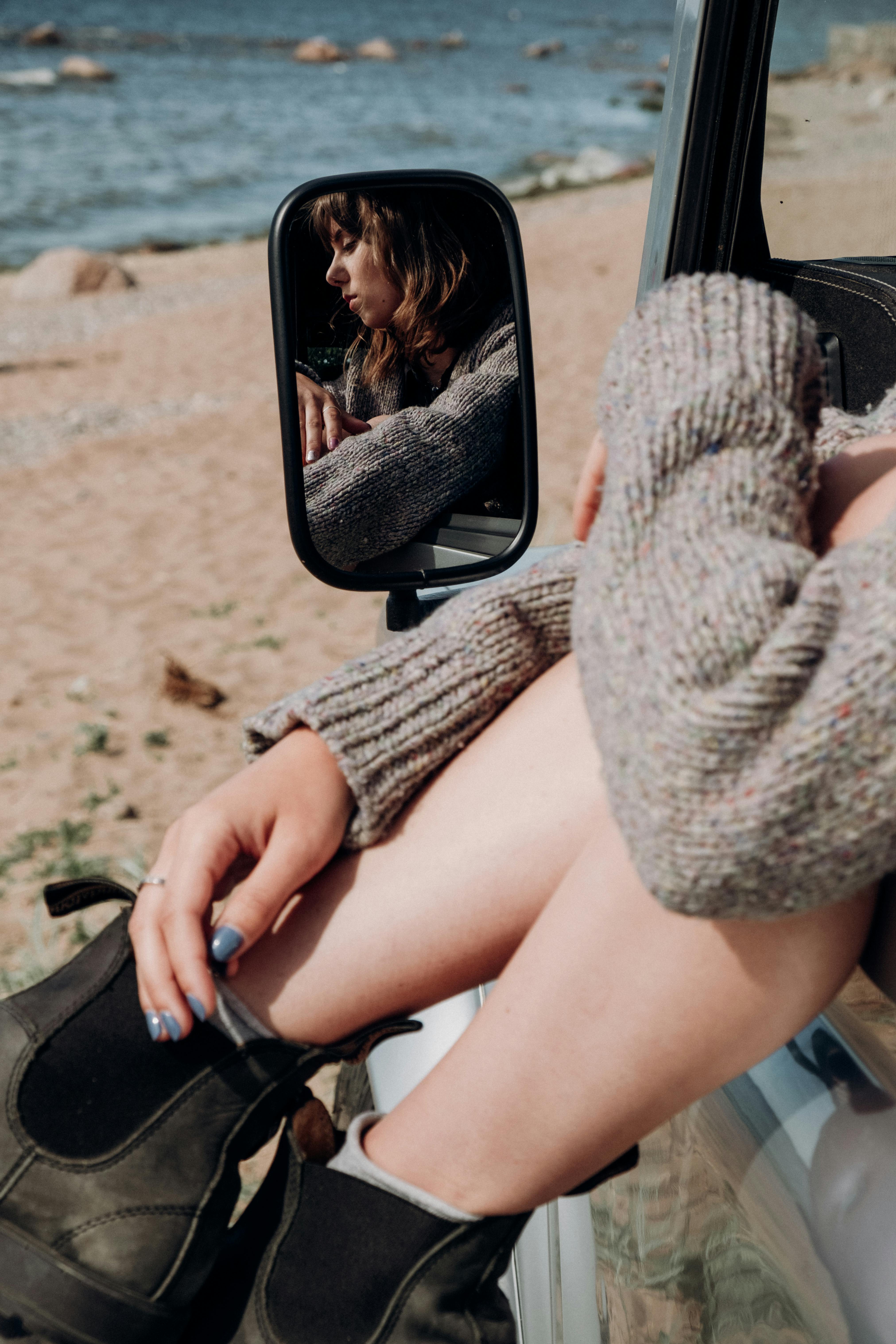 阳光明媚的海滩上，一名女子在汽车后视镜中的倒影显得格外宁静