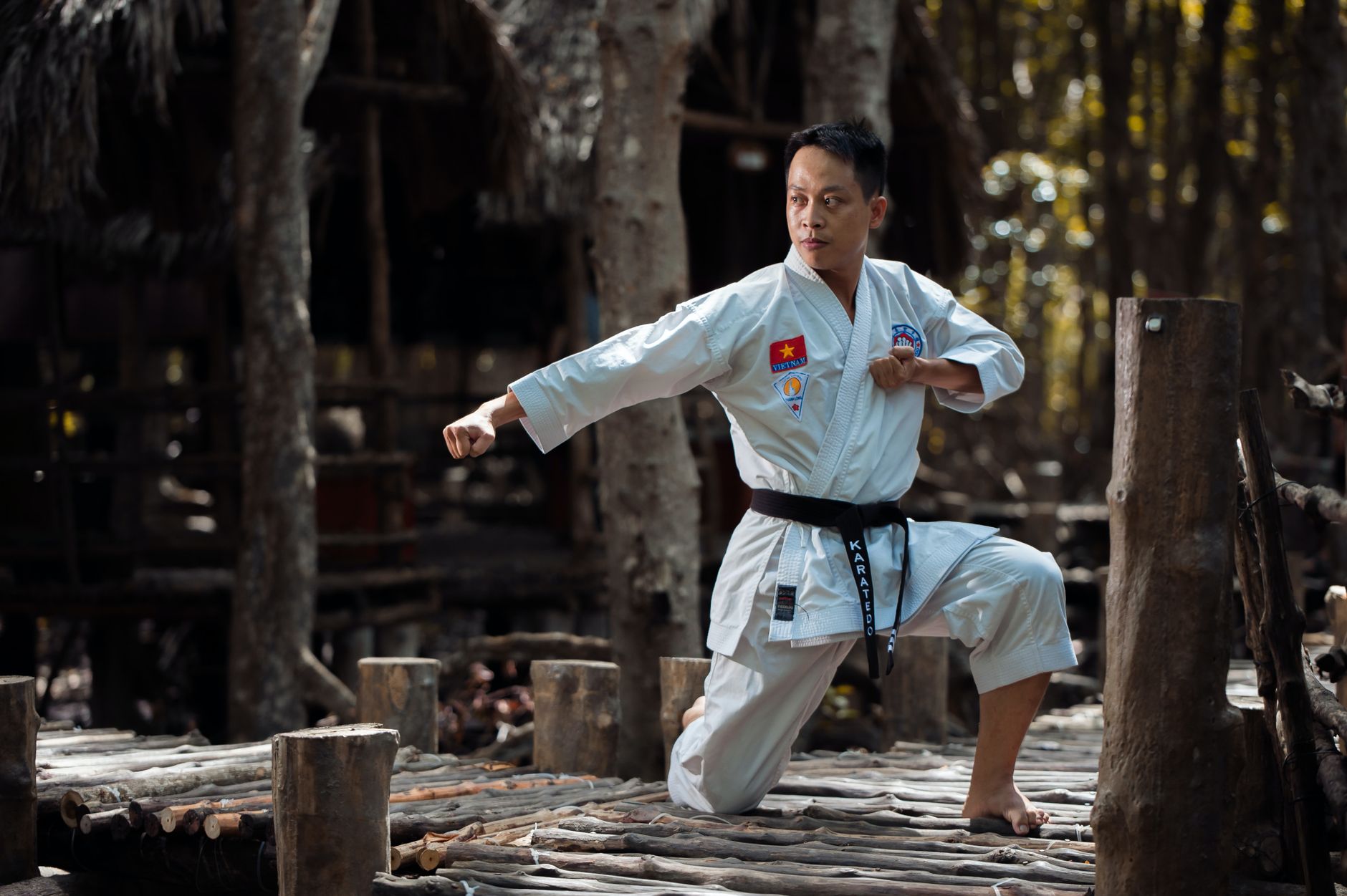 A focused martial artist demonstrating karate techniques outdoors in a Vietnamese forest setting.