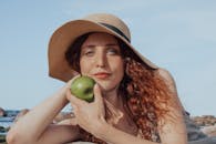 一位戴着帽子的轻松女士拿着一个青苹果，享受着阳光明媚的海滩日子