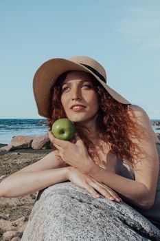 一名戴着太阳帽的女子在阳光明媚的海滩上拿着一个青苹果摆姿势