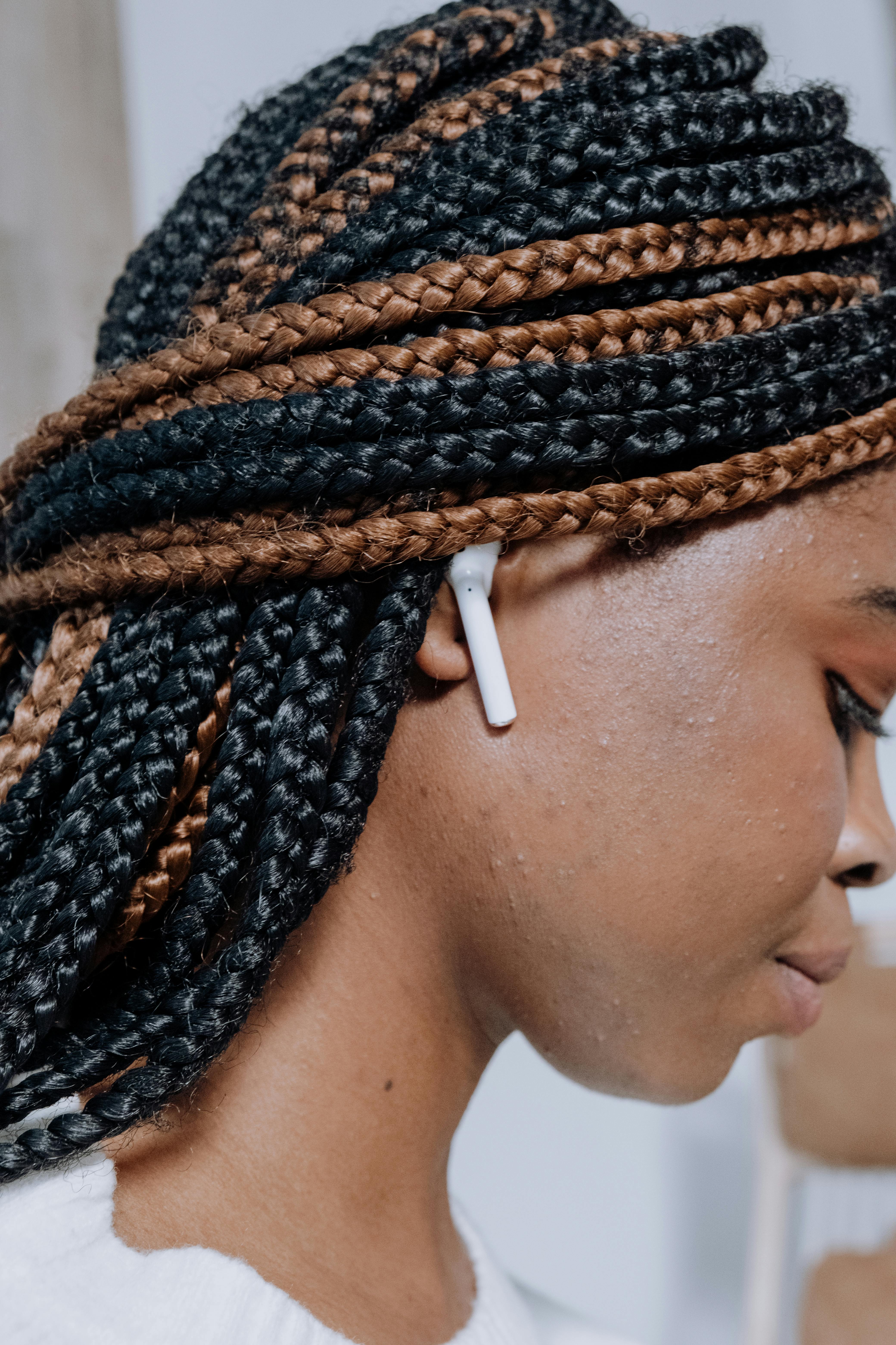 Profile of a woman with braided hairstyle wearing AirPods, showcasing modern technology and style.