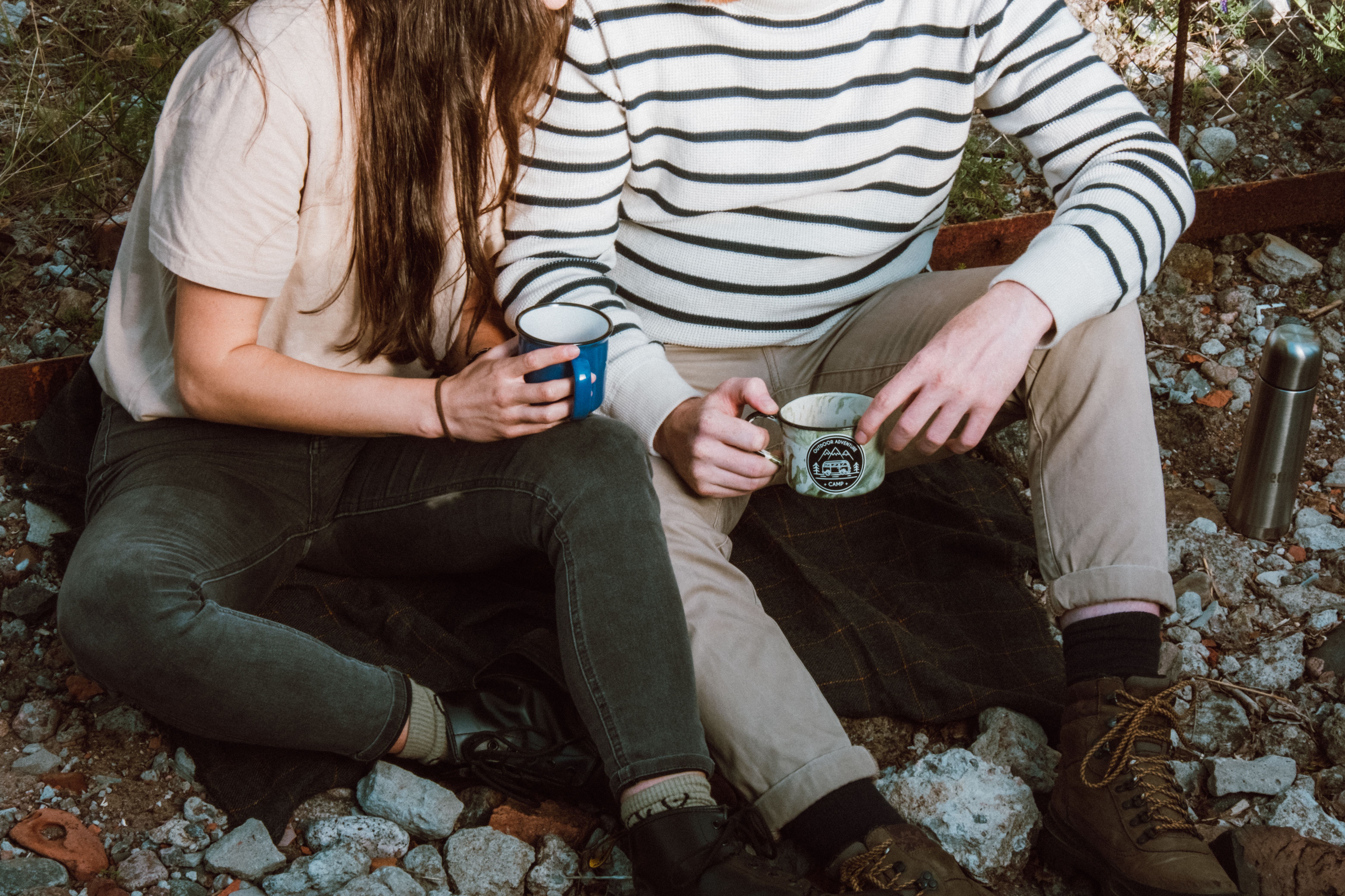 A couple enjoying a peaceful moment outdoors, holding coffee mugs, sitting on a rocky surface.