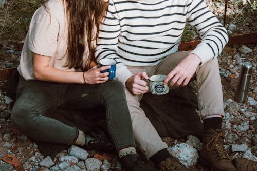 Couple Holding Cups While Sitting on the Ground