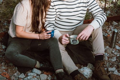 Free A couple enjoying a peaceful moment outdoors, holding coffee mugs, sitting on a rocky surface. Stock Photo