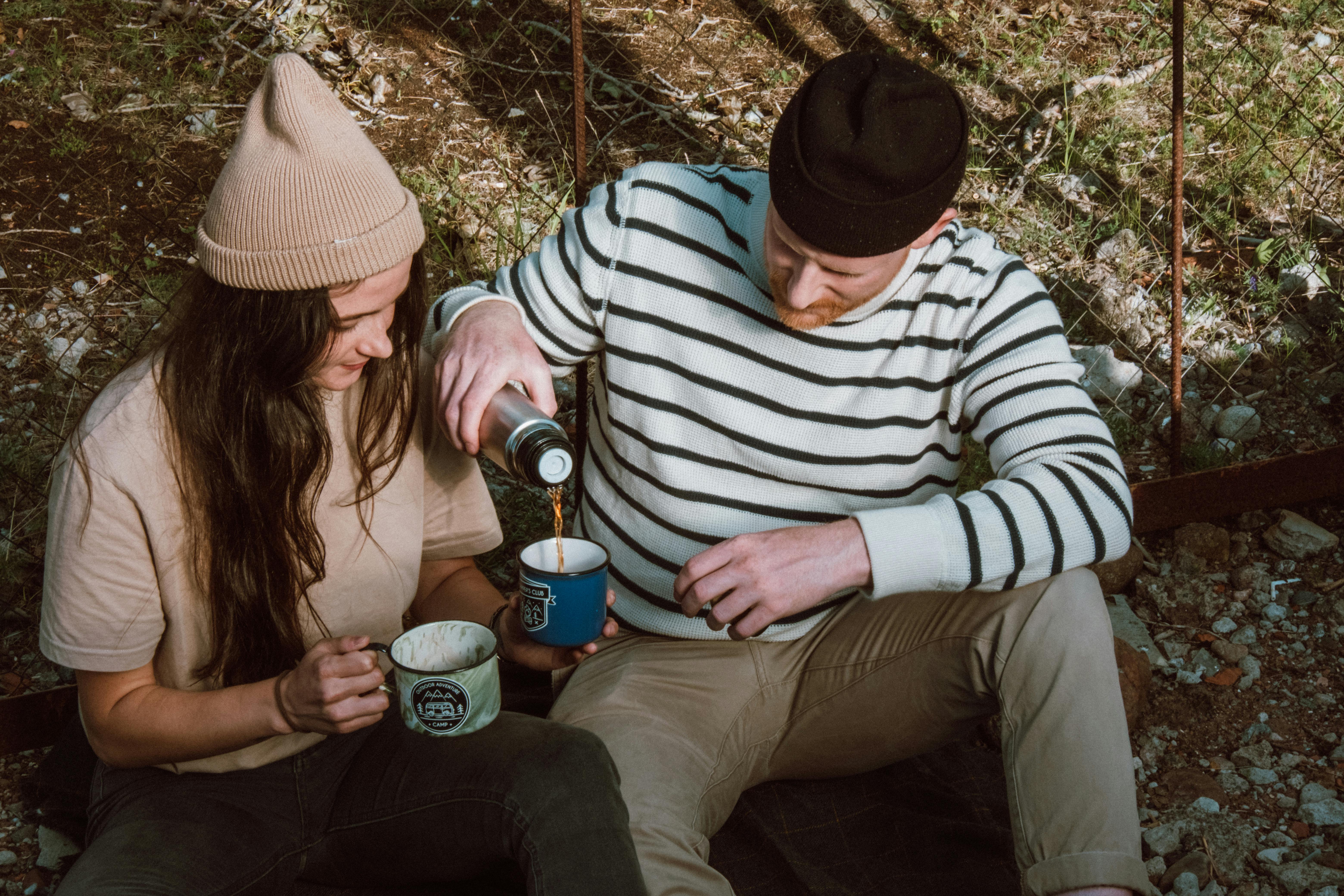 Couple sitting outdoors, enjoying hot beverages from mugs, perfect for lifestyle themes.