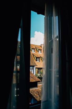 Captivating view of historic rooftops through a window draped with curtains.