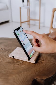 Hand interacting with smartphone on wooden stand indoors.