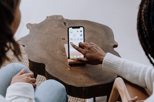 Free Two individuals use a smartphone together indoors, focused on screen interaction on a wooden table. Stock Photo