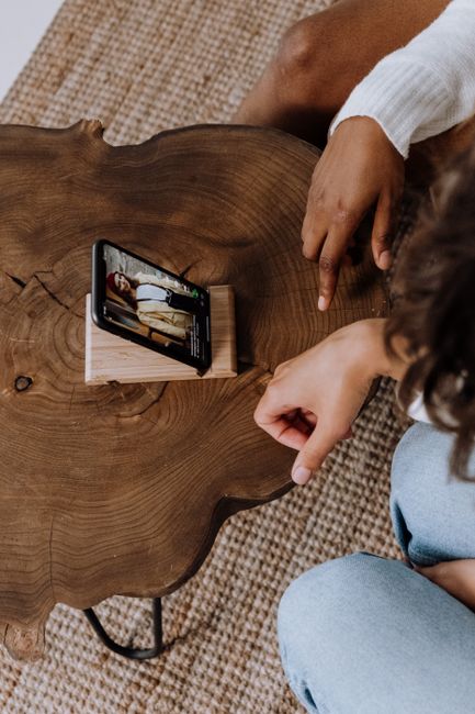 Top view of hands interacting with a smartphone on a wooden table.