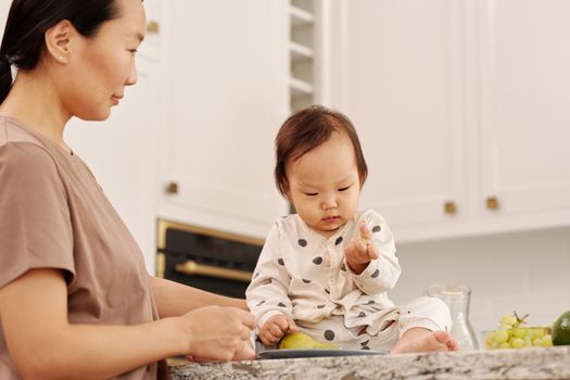 在明亮而温暖的厨房里，一位亚洲母亲正与女婴分享着温柔的时刻
