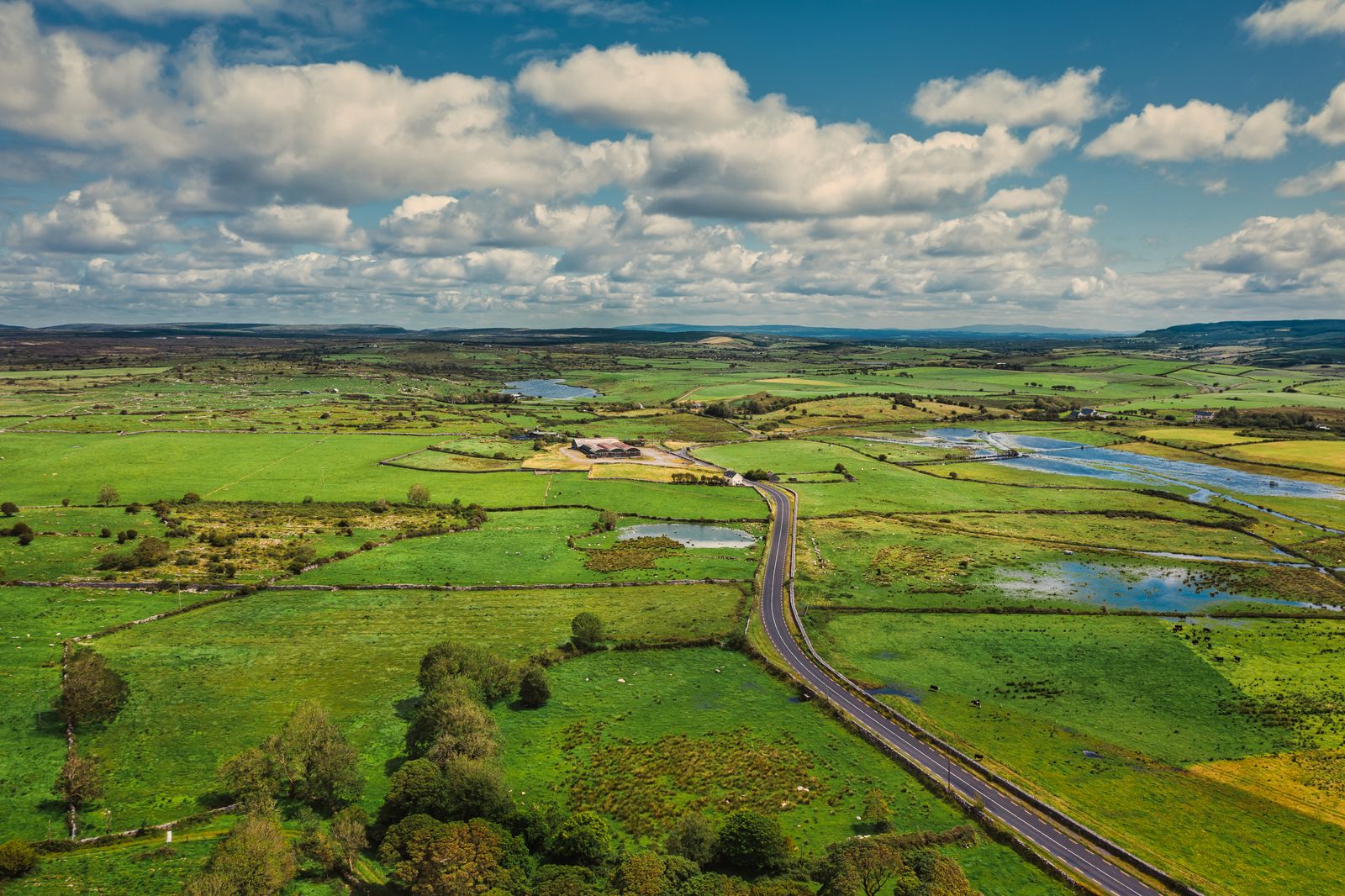 Aerial view of the green countryside and long road in County Clare, Ireland, under a partly cloudy sky