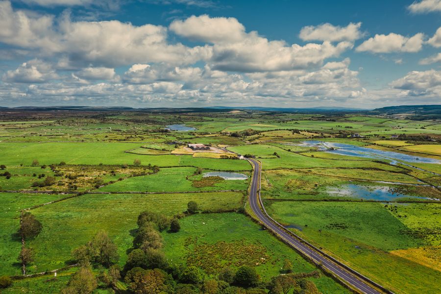 Aerial view of the green countryside and long road in County Clare, Ireland, under a partly cloudy sky