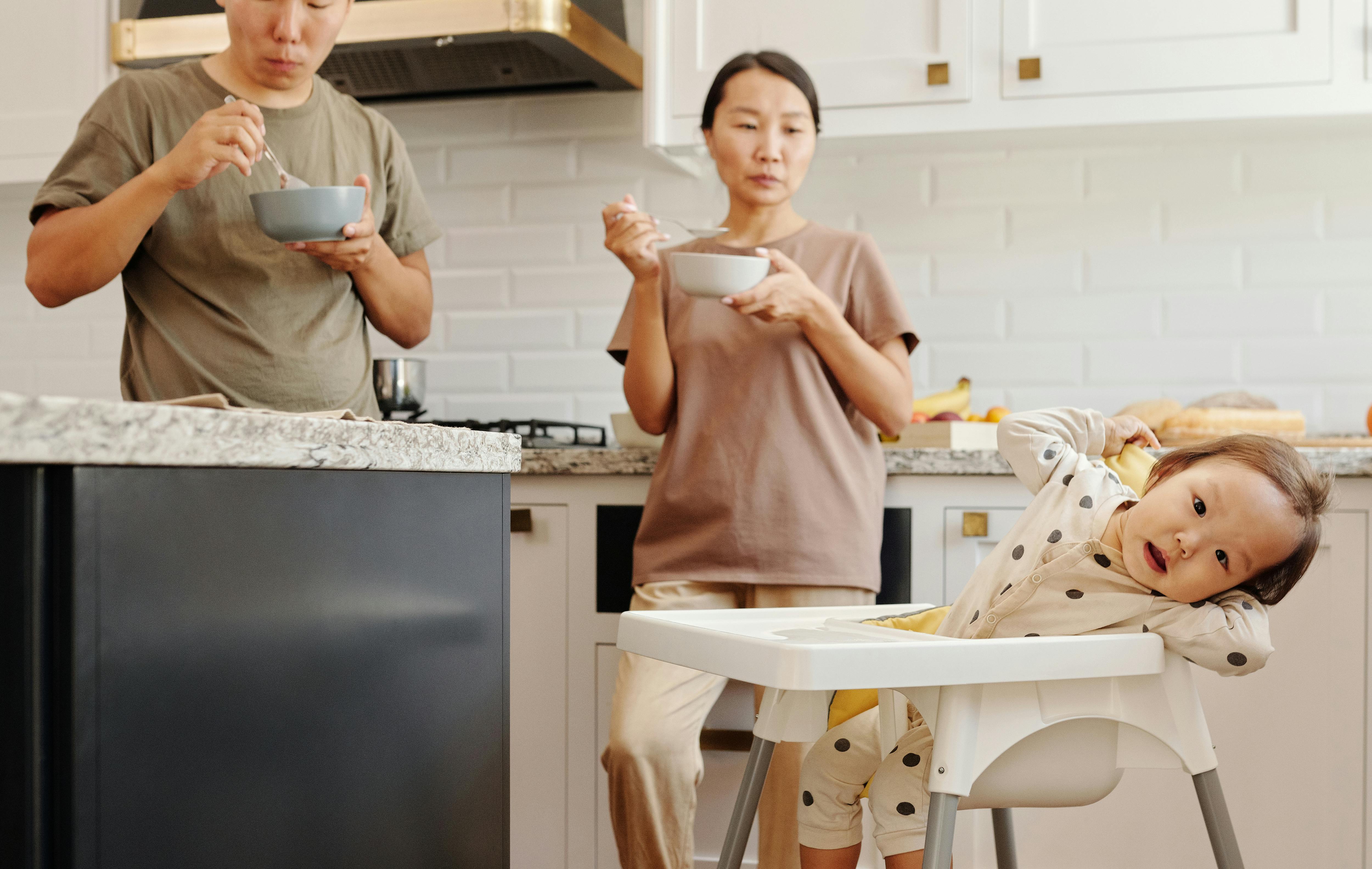Asian family having breakfast together in a cozy kitchen setting, featuring parents and a toddler.