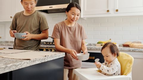 Asian family enjoying mealtime in home kitchen with baby in high chair.