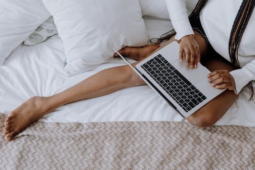 Free A woman with braids working on a laptop while seated on a bed, showcasing a modern and relaxed lifestyle. Stock Photo