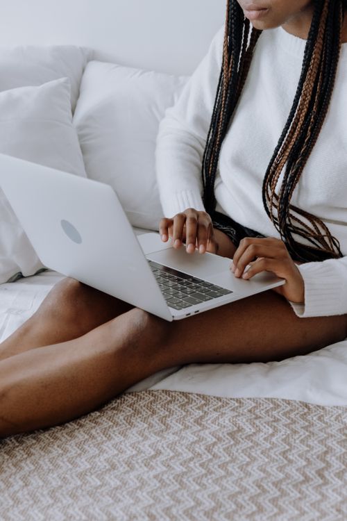 Free Young woman typing on laptop while sitting on bed in a cozy home setting. Ideal for technology and lifestyle themes. Stock Photo