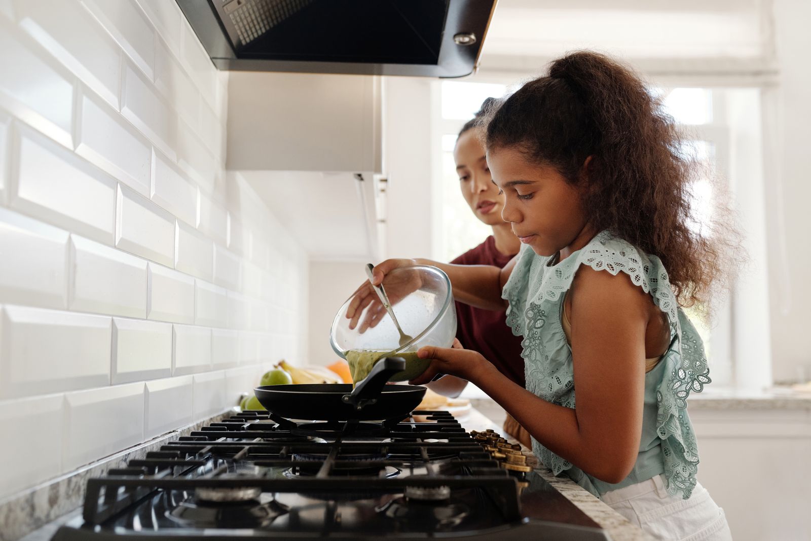 A mother and daughter enjoying cooking together in a bright kitchen setting.