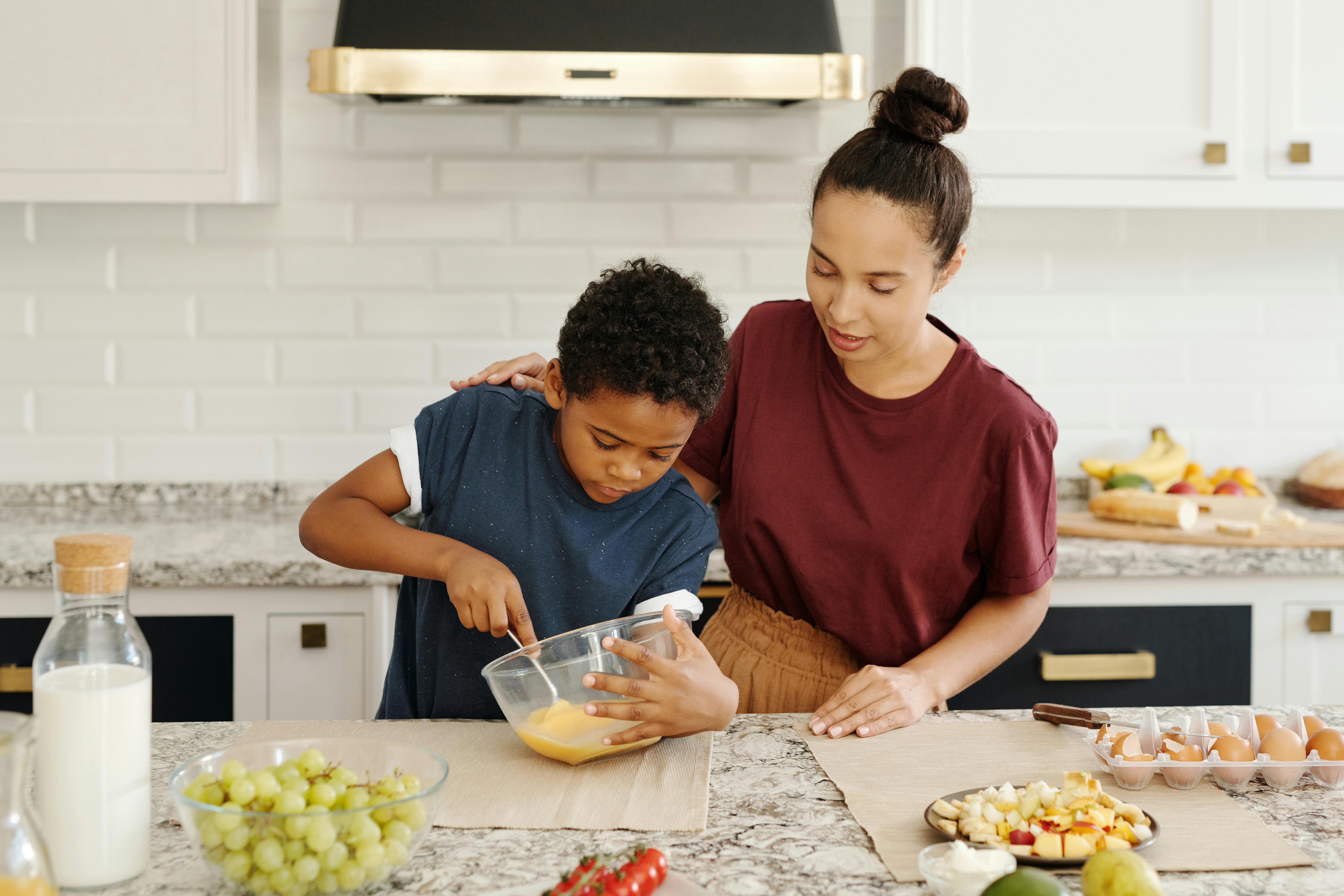 a mother looking at her son bait the egg on the bowl