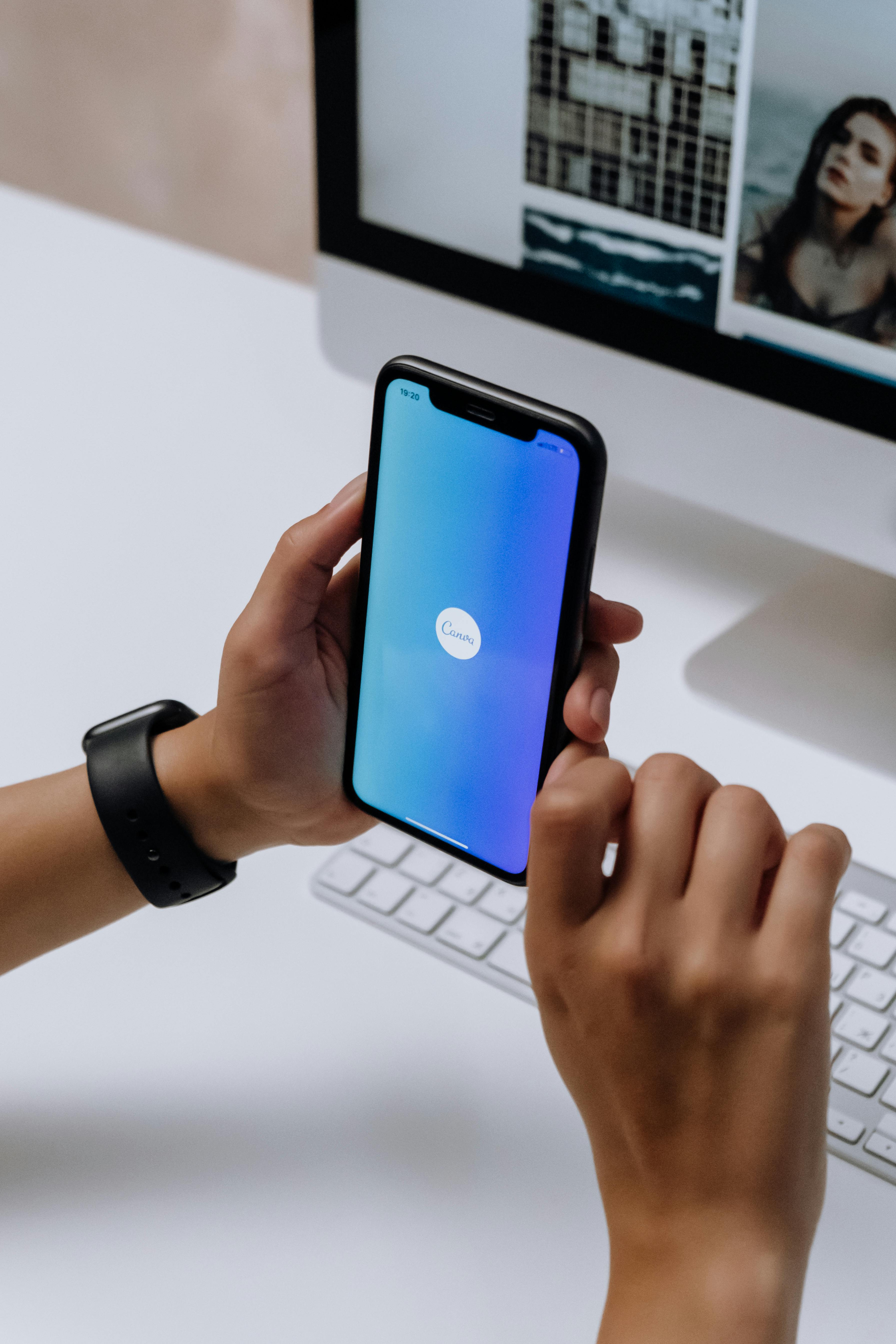 holding a smartphone in front of an imac