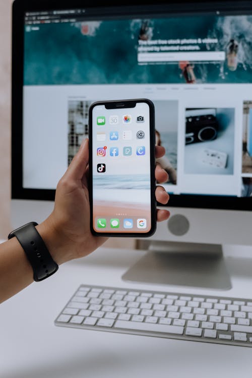 Free Holding a Smartphone in front of an Imac Stock Photo