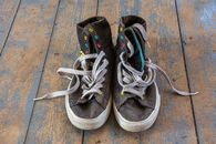 Old high top sneakers with colorful eyelets on a rustic wooden floor.
