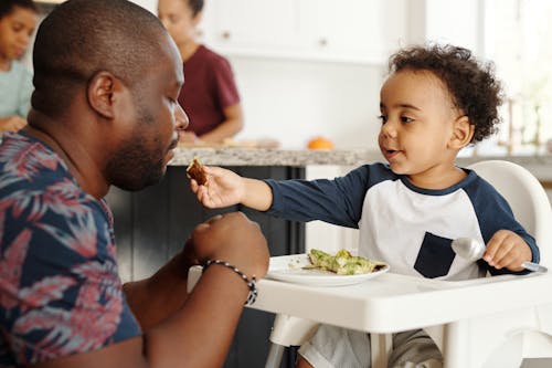 Free Boy Feeding Father in Kitchen Stock Photo