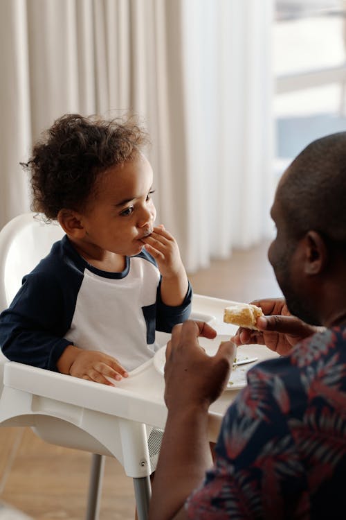 Free Man Feeding Baby in Feeding Chair Stock Photo