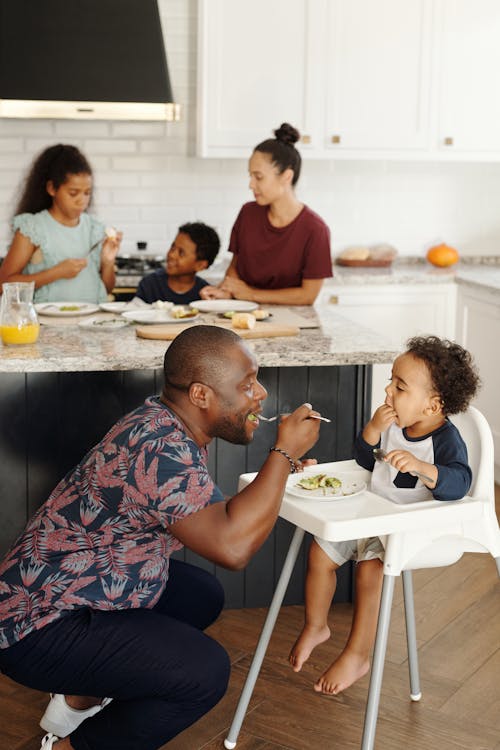 Free Big Family in Kitchen and Man Feeding Baby in Feeding Chair Stock Photo