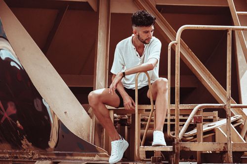 Free A fashionable man in a white t-shirt sitting on an industrial structure outdoors. Stock Photo
