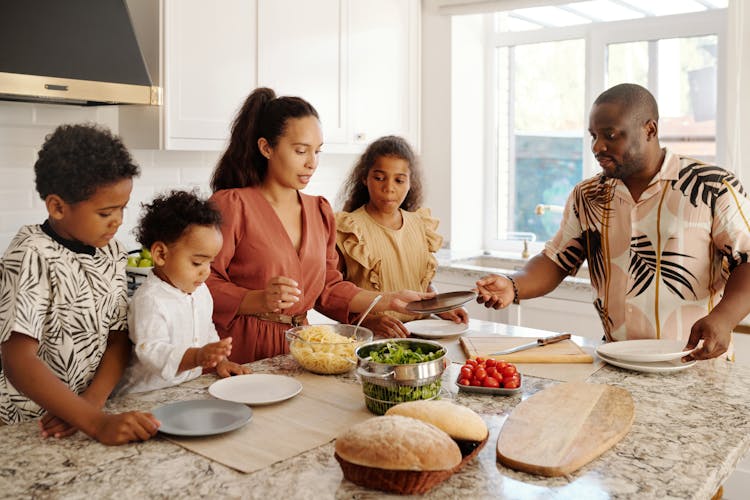 A Man And Woman Preparing Foods In The Kitchen With Their Kids