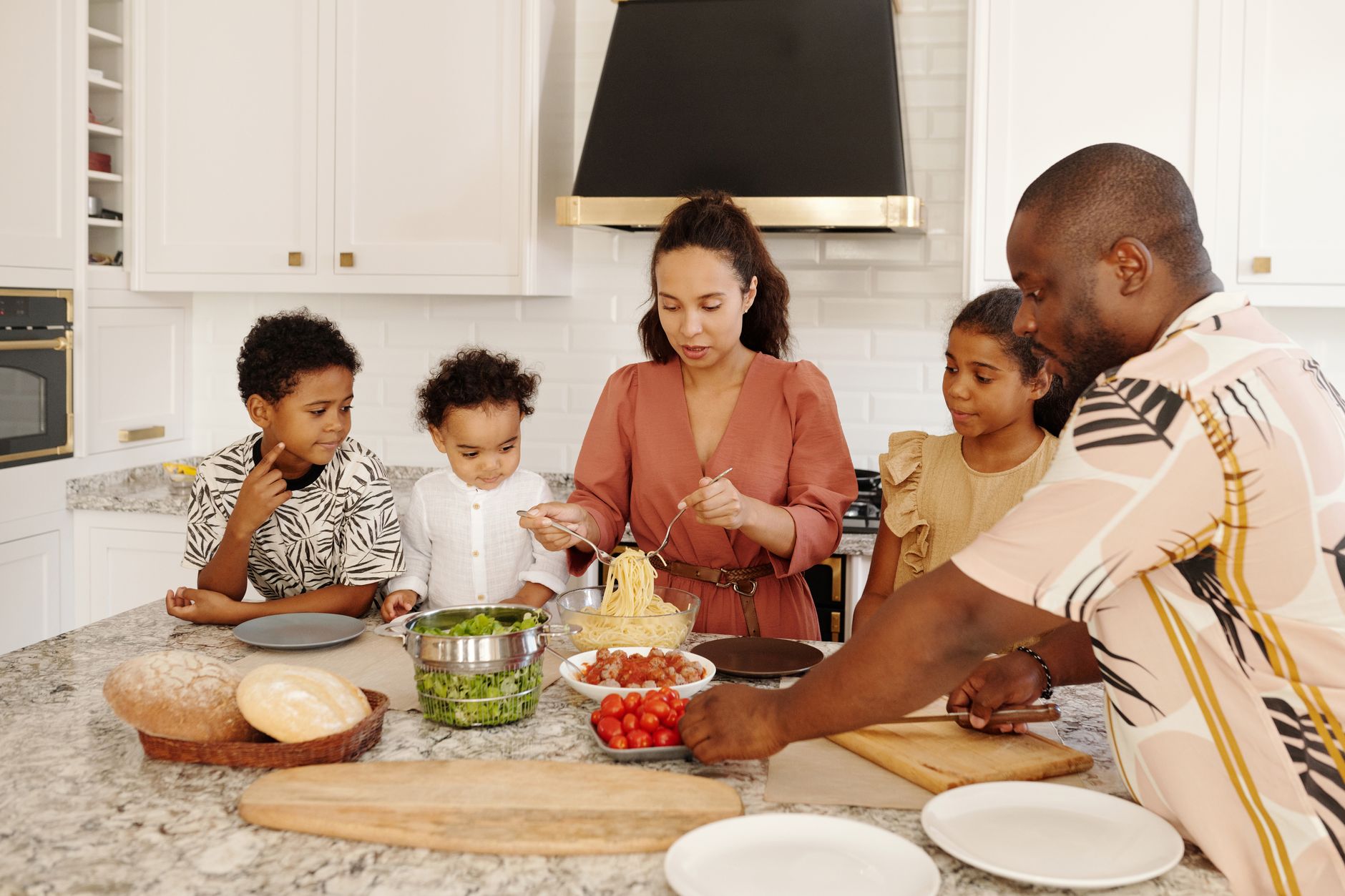 健康飲食與時間管理衝突的實用解法 A diverse family prepares pasta in a modern white kitchen, conveying unity and culinary art.