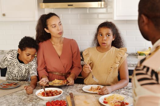 A family gathers around the kitchen table enjoying a pasta meal together.