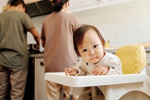 可爱的幼儿坐在高脚椅上，父母在厨房里准备食物
