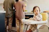 父母在厨房准备食物时，蹒跚学步的孩子正坐在高脚椅上享受早餐