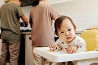 可爱的幼儿穿着圆点服装，坐在高脚椅上，父母则在厨房做饭