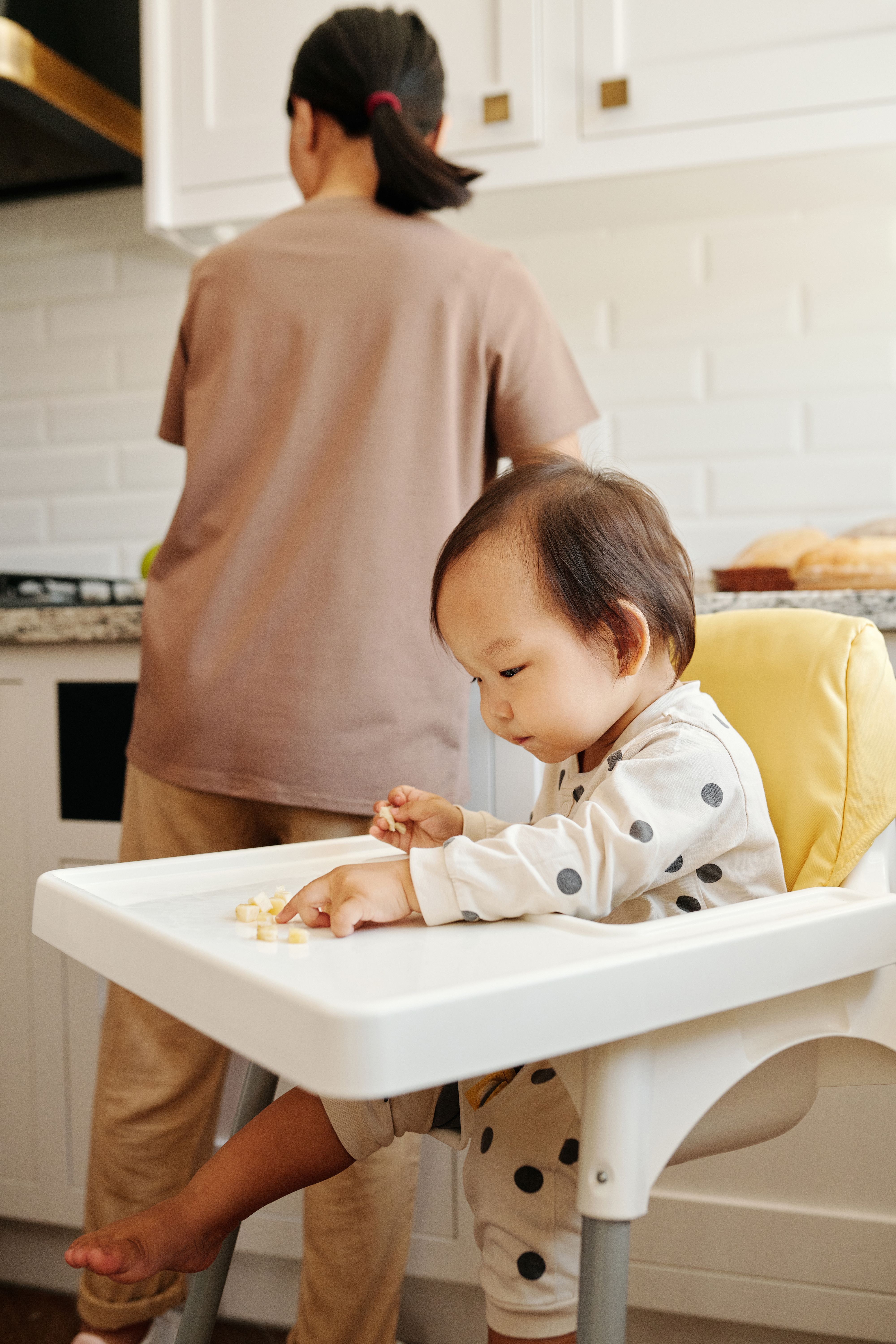 可爱的幼儿在舒适的厨房里享用零食，旁边有护理人员照看