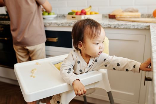 穿着圆点服装的可爱幼儿和家人一起，从厨房的高脚椅上探出身来
