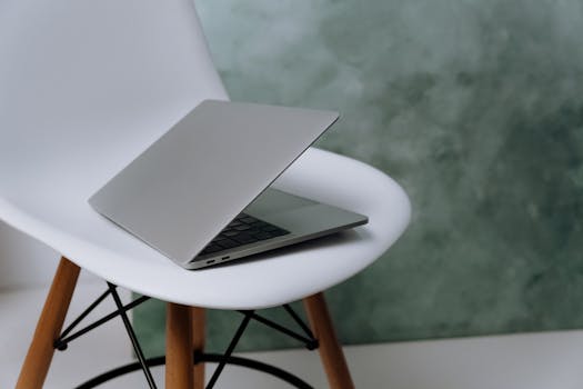 Sleek laptop on a stylish white chair against a green background, showcasing minimalism.