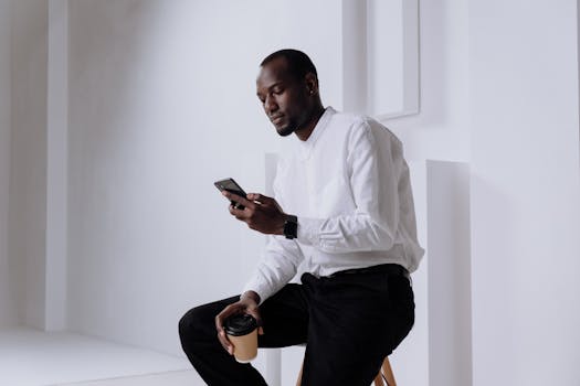 Businessman in a white shirt uses a smartphone indoors with a coffee cup.