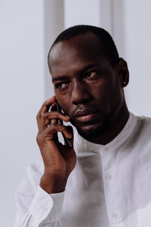 Free Serious-looking man in white shirt making a phone call indoors, focusing intently. Stock Photo