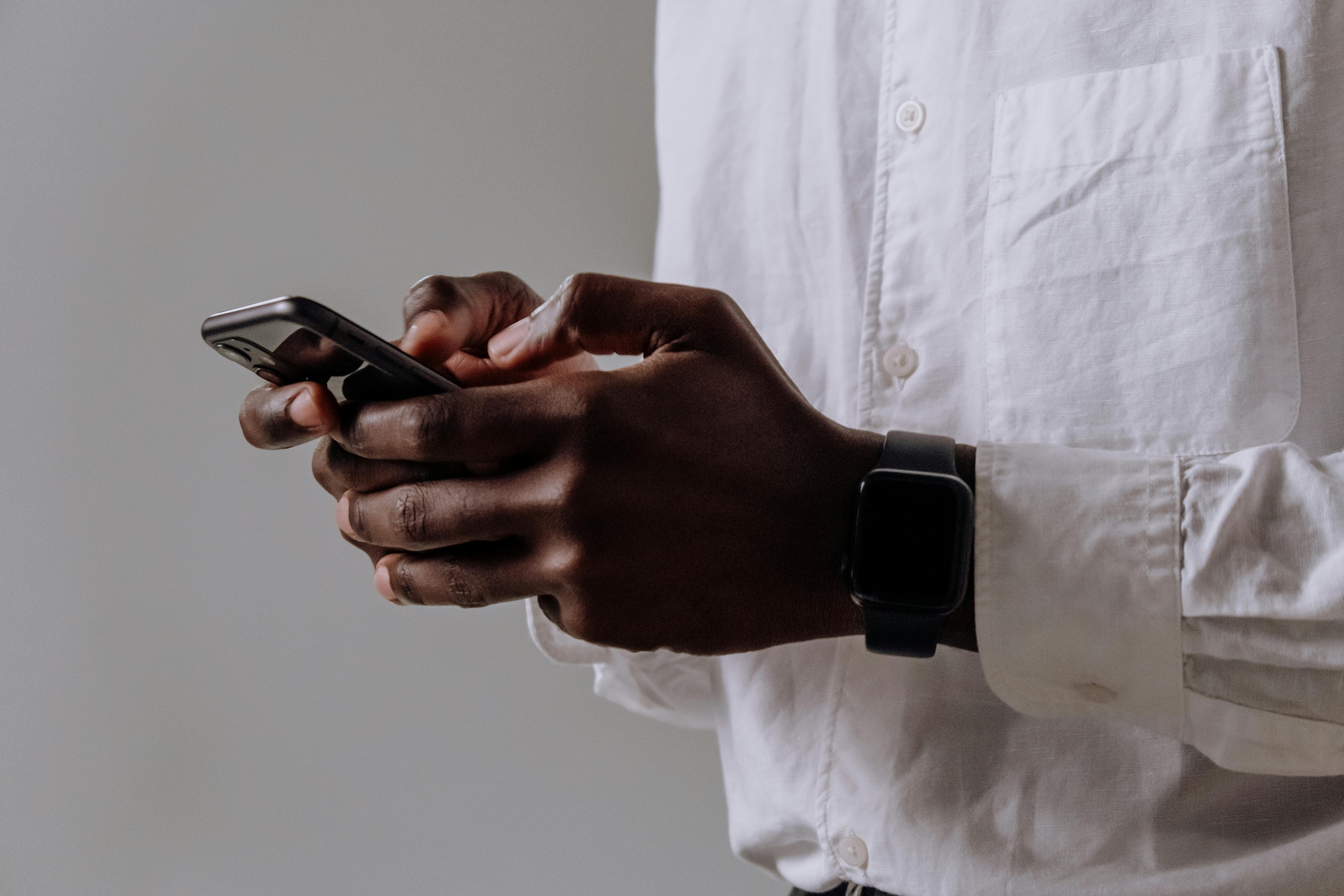 person in white dress shirt holding black smartphone