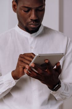 一名男子身穿白衬衫，在室内使用平板电脑，展现了现代技术的应用